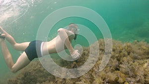 A thin man with a beard in a mask swims underwater, waving his arms. Close-up.