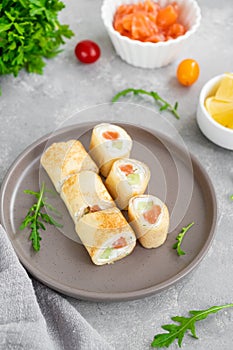 Thin pancake rolls or crepes rolls with smoked salmon, cream cheese, cucumber and dill on a gray concrete background.