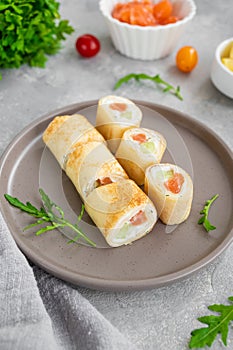 Thin pancake rolls or crepes rolls with smoked salmon, cream cheese, cucumber and dill on a gray concrete background.