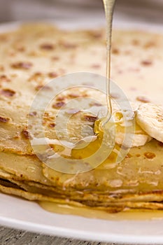 Thin pancakes with banana and honey. Maslenitsa. Russian pancakes on a light wooden background. In a rustic style.