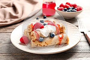 Thin pancakes served with syrup, cream and berries
