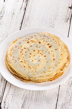 Thin pancakes on a white plate. Maslenitsa. Russian pancakes on a light wooden background. In a rustic style.