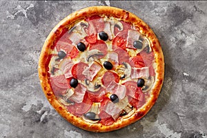 Thin pizza with bacon, salami, mushrooms, tomatoes and black olives on gray stone surface