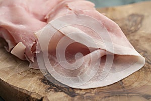 Thin slices of prosciutto cotto on olive wood board photo