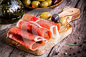 Thin slices of prosciutto with mixed olives on a cutting board