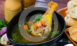 Thin soup with chicken leg in black bowl