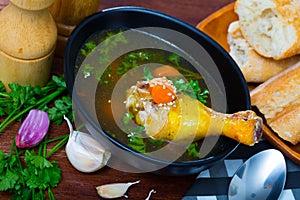 Thin soup with chicken leg in black bowl