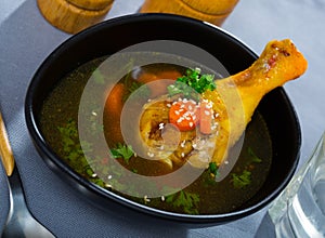 Thin soup with chicken leg in black bowl