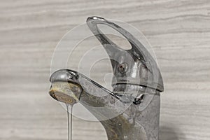 A thin stream of hard water flows from an old tap aerator.