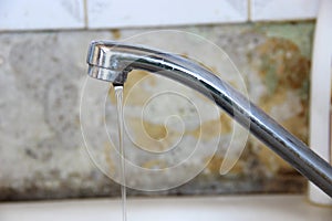 a thin stream of water flows from the tap, silver colored kitchen faucet on old wall background