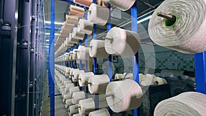 Thin threads spooling onto bobbins on industrial rack.