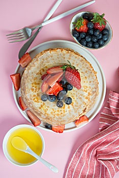 Thin traditional Russian pancakes on a trendy pink background with berries and honey. Vertical photo, top view