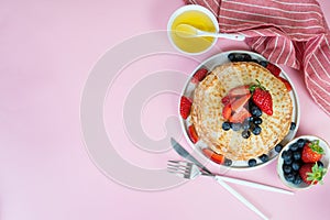 Thin traditional Russian pancakes on a trendy pink background with berries and honey. Top view, copy space