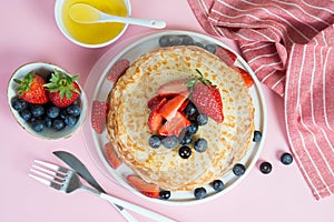 Thin traditional Russian pancakes on a trendy pink background with berries and honey. H orizontal p hoto, c lo s e- up