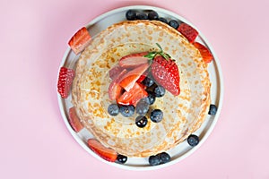 Thin traditional Russian pancakes on a trendy pink background with berries and honey. Horizontal photo, top view