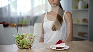 Thin woman choosing between cake and salad, healthy diet vs high-calorie food