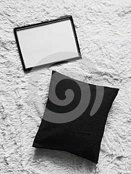 Thin wooden frame with blank copyspace as poster photo print mockup, black cushion pillow and fluffy white blanket, flat