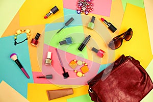 Things from open lady purse. Cosmetics and women`s accessories fell out of red handbag on colourful background.