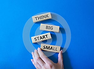 Think big start small symbol. Concept words Think big start small on wooden blocks. Beautiful blue background. Businessman hand.