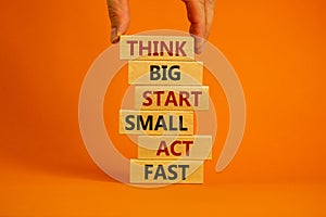 Think big start small symbol. Words `Think big start small act fast` on wooden blocks on a beautiful orange background.