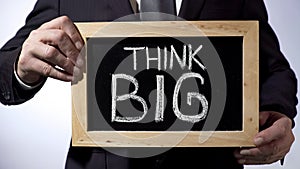 Think big written on blackboard, male in suit holding sign, motivational concept