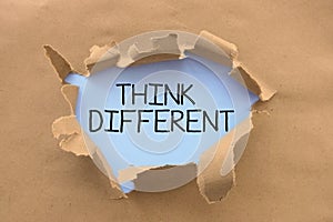 Think different advice handwritten on white page, behind torn brown paper or cardboard