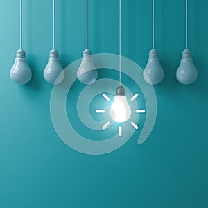 One hanging glowing idea light bulb standing out from dim unlit bulbs on green pastel color wall background
