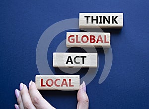 Think global act local symbol. Wooden blocks with words Think global act local. Beautiful deep blue background. Businessman hand.