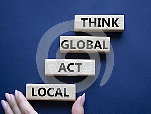 Think global act local symbol. Wooden blocks with words Think global act local . Beautiful deep blue background. Businessman hand