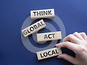 Think global act local symbol. Wooden blocks with words Think global act local . Beautiful deep blue background. Businessman hand