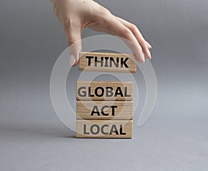 Think global act local symbol. Wooden blocks with words Think global act local. Beautiful grey background. Businessman hand.