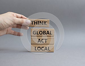 Think global act local symbol. Wooden blocks with words Think global act local . Beautiful grey background. Businessman hand.