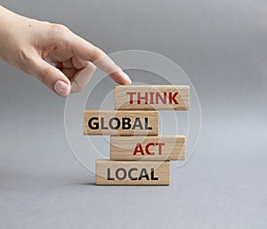 Think global act local symbol. Wooden blocks with words Think global act local . Beautiful grey background. Businessman hand.