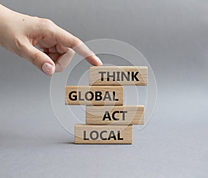 Think global act local symbol. Wooden blocks with words Think global act local . Beautiful grey background. Businessman hand.