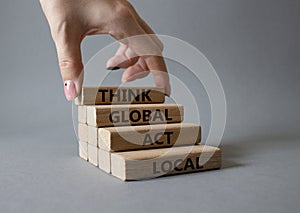 Think global act local symbol. Wooden blocks with words Think global act local . Beautiful grey background. Businessman hand.