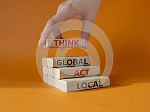 Think global act local symbol. Wooden blocks with words Think global act local. Beautiful orange background. Businessman hand.