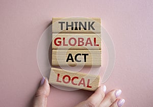 Think global act local symbol. Wooden blocks with words Think global act local. Beautiful pink background. Businessman hand.