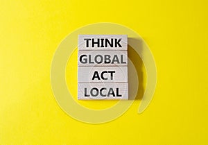 Think global act local symbol. Wooden blocks with words Think global act local. Beautiful yellow background. Business and Think