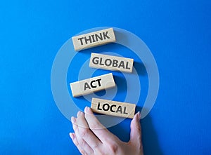 Think global act local symbol. Wooden blocks with words Think global act local. Businessman hand. Beautiful blue background.