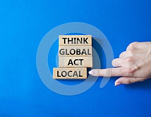 Think global act local symbol. Wooden blocks with words Think global act local. Businessman hand. Beautiful blue background.