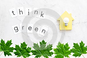 Think green text with house toy, lamp, green maple leaves on marble background top view