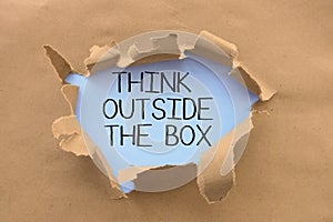 Think outside the box saying or advice handwritten on white page, behind torn brown paper or cardboard