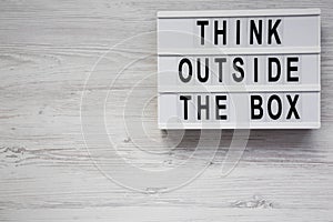 `Think outside the box` words on a modern board on a white wooden background, top view. Flat lay, overhead, from above. Copy spa