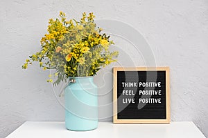 Think positive, feel positive, live positive. Motivational quote on letter board and bouquet yellow flowers on white table against