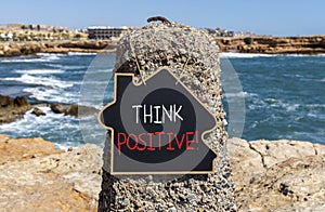 Think positive symbol. Concept words Think positive on beautiful black chalk blackboard. Beautiful stone sea blue sky background.