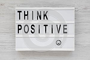 `Think positive` words on a lightbox on a white wooden background, top view. Overhead, from above, flat lay. Close-up