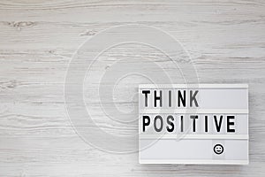 `Think positive` words on a lightbox on a white wooden background, top view. Overhead, from above, flat lay. Copy space