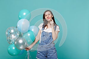 Thinkful young woman in denim clothes looking up put hand prop up on chin celebrating hold colorful air balloons