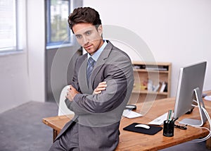 Thinking back on his career. A handsome young businessman sitting on his desk with his arms crossed.