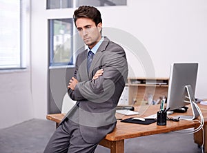 Thinking back on the past financial quarter. A handsome young businessman sitting on his desk with his arms crossed.